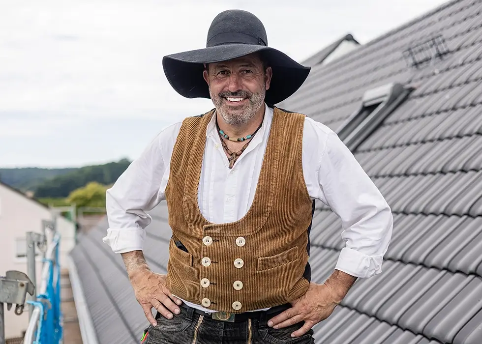 Ein Zimmermann in Zunftbekleidung steht auf dem Dach